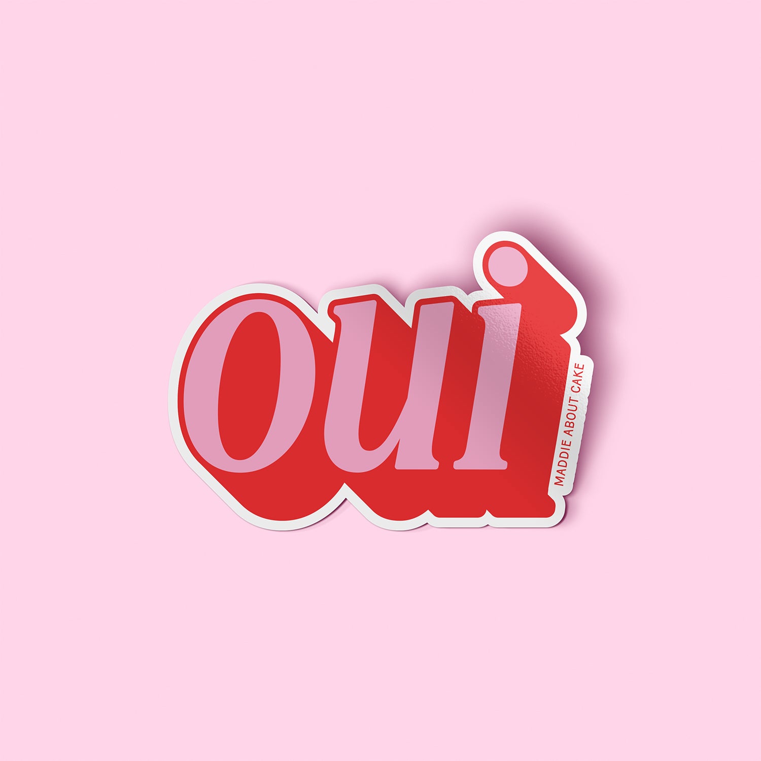 Pink and red decorative sticker that says "oui" in an italicized serif font. The text is pink with red shadow so it appears 3D. The sticker is laying on a light pink background.