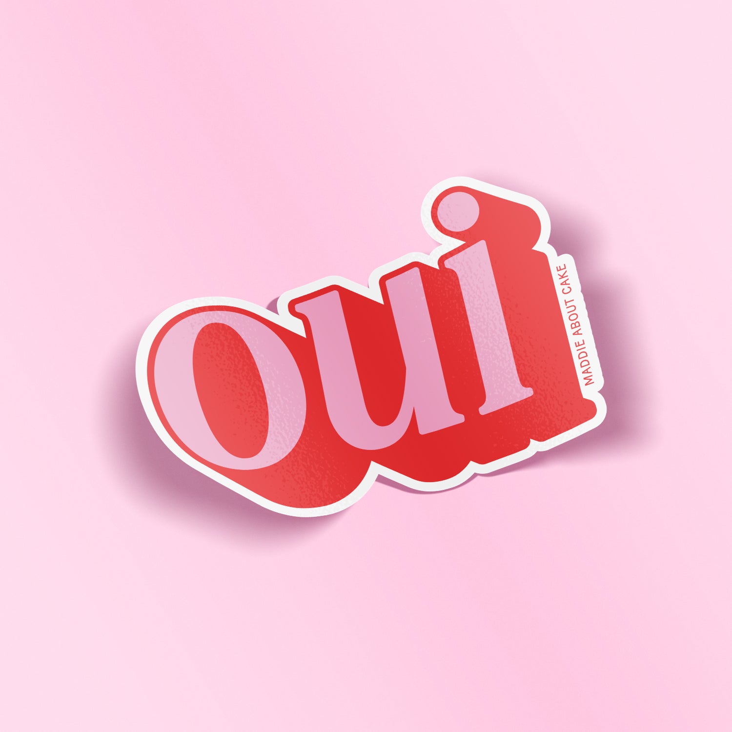 Pink and red decorative sticker that says "oui" in an italicized serif font. The text is pink with red shadow so it appears 3D. The sticker is laying on a light pink background.