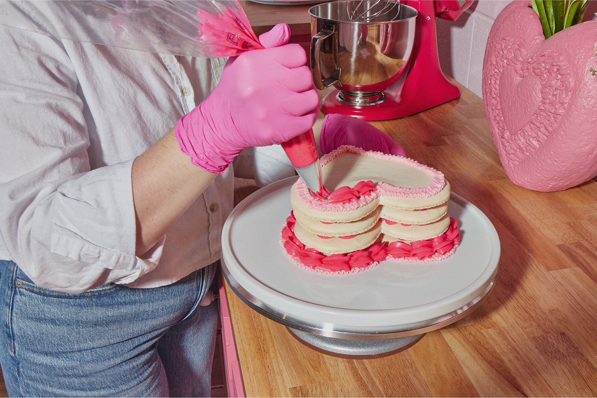 Close up of Maddie, founder and head baker at Maddie About Cake, piping pink icing onto one of her signature heart shaped macaron layer cakes.