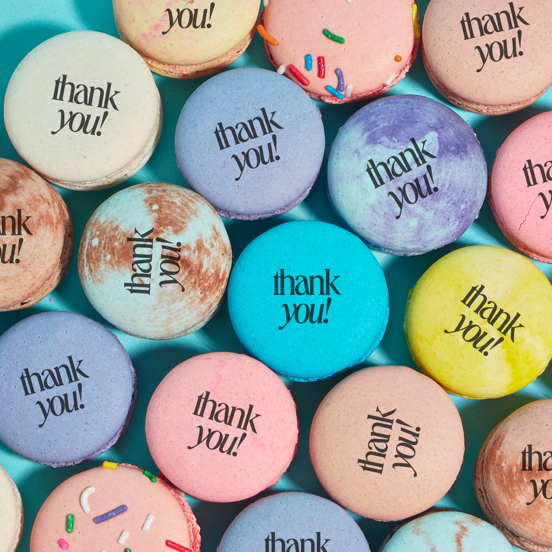 Overhead shot of various macarons colors and flavors printed with the words "thank you" in black text.